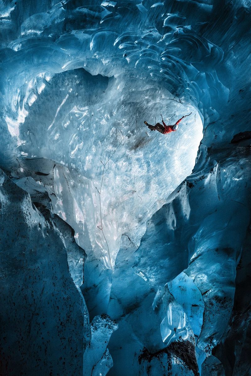 An ice climber ascends the blue walls of a heart-shaped ice cave.