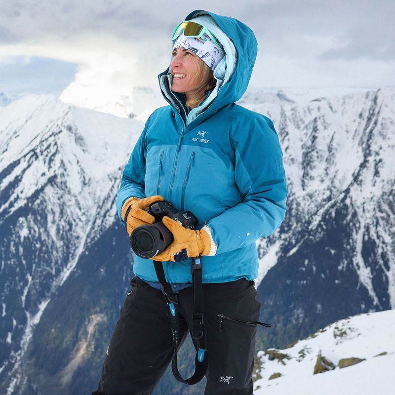 A portrait of Canon Ambassador Julia Roger-Veyer standing in front of snow-covered peaks and holding a Canon camera, taken by Eliott Fettweis.
