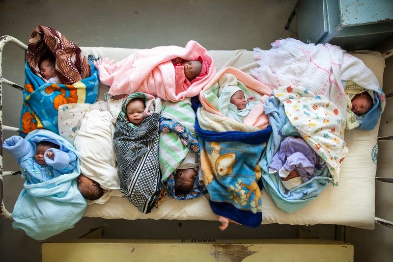 Multiple babies lie swaddled in patterned fabrics, on a small hospital bed. 