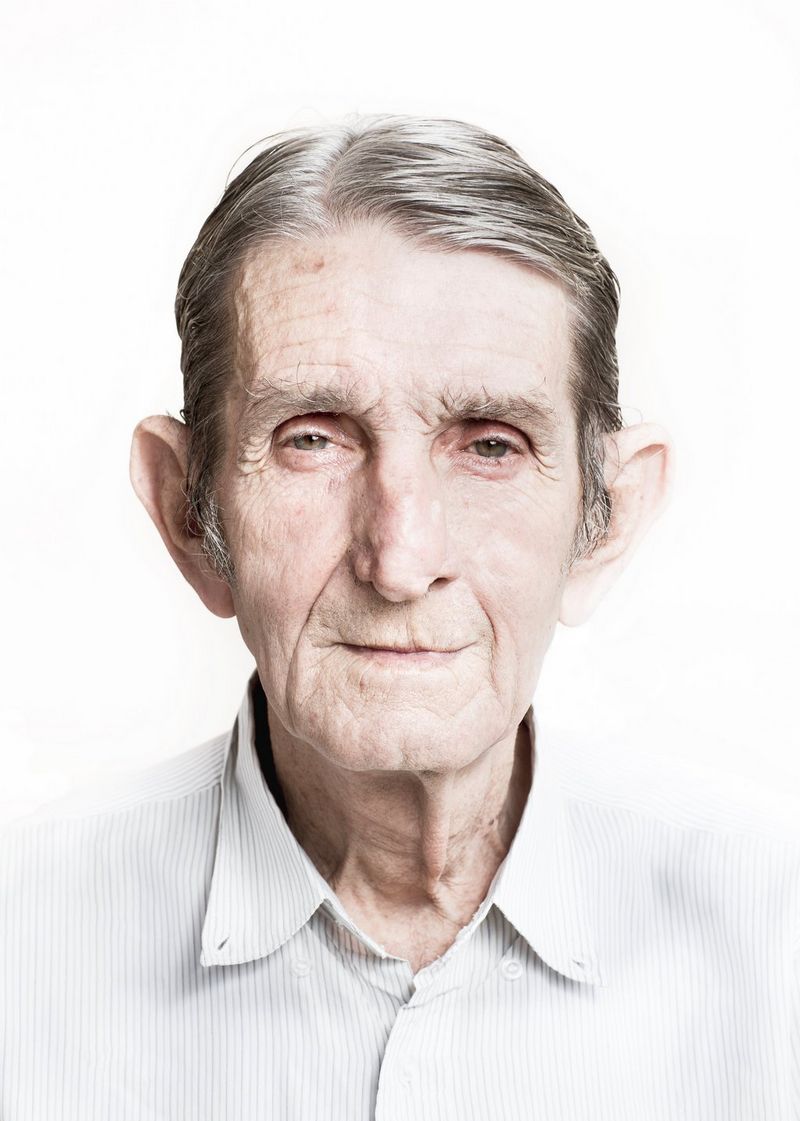 An older man looks directly at the camera. His greying hair is neatly combed and he wears a pinstripe shirt.