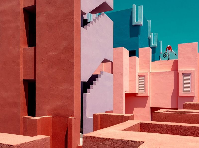 A BMX rider performs a trick on the colourful walls of a geometrically designed building.