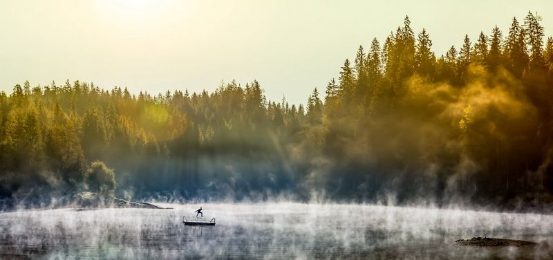 In the distance, a skateboarder practises stunts on a bathing platform in the centre of a lake. Early-morning mist rises all around him.