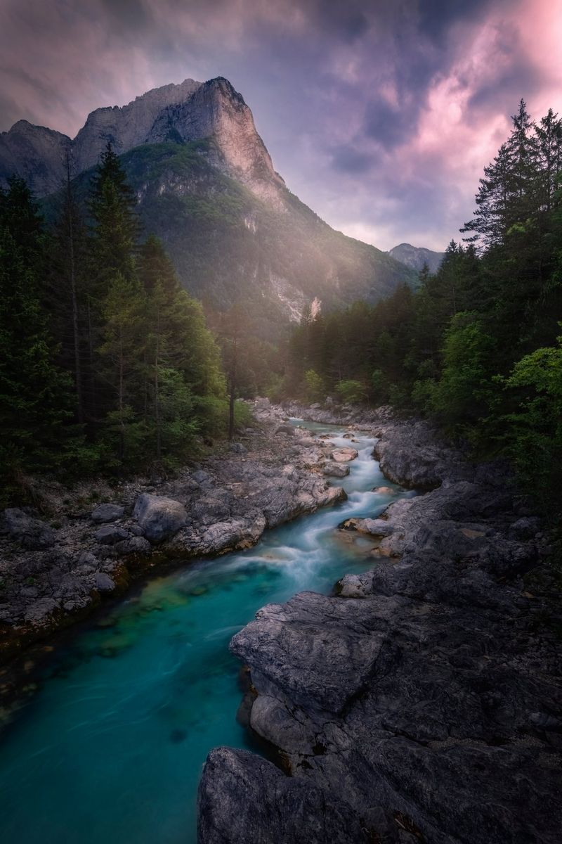 Photographed with a long exposure, the Soča river flows through an alpine woodland, a single mountain peak visible in the background. Taken on a Canon EOS R5 by Canon Ambassador Luka Vunduk.