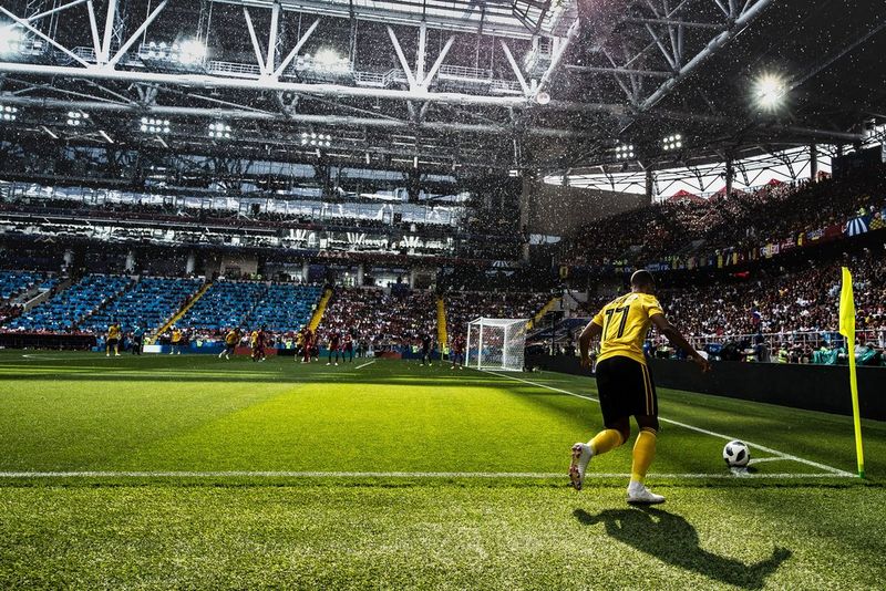 A football player in a yellow top and black shorts prepares to take a corner during an international match.