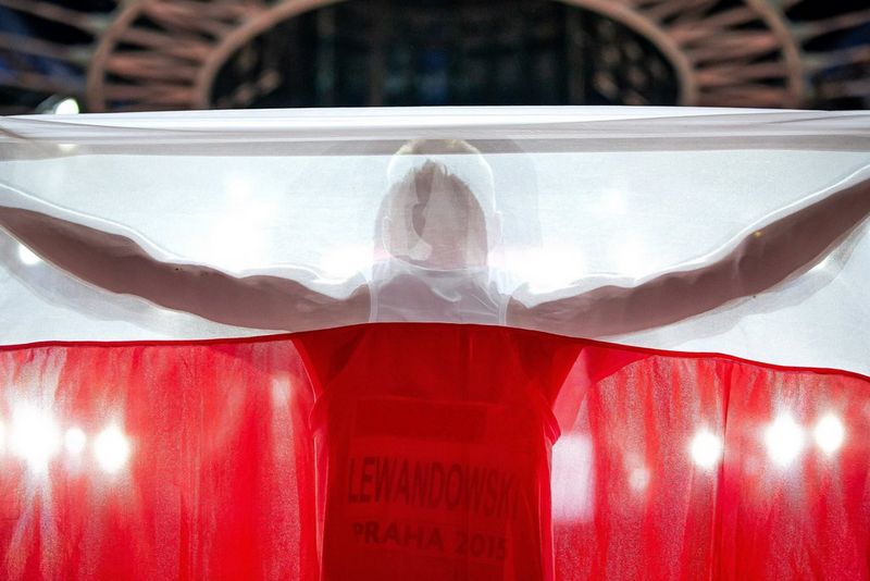 The back of a runner, wearing a racing vest and bib, obscured by the Polish flag of red and white he's holding aloft.