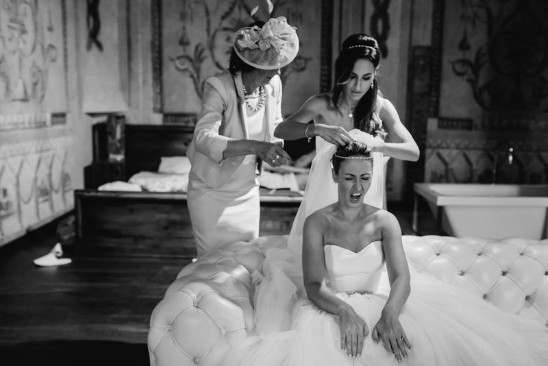 Image en noir et blanc d'une mariée faisant une grimace pendant qu'une demoiselle d'honneur ajuste son voile sous le regard de sa mère. Photo prise par Malachite Meadow avec un Canon EOS 5D Mark III.