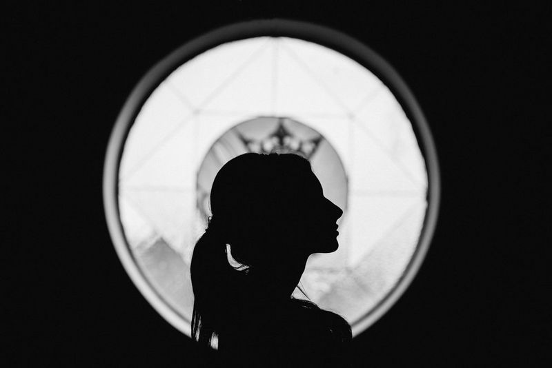 Silhouette en noir et blanc du profil d'une mariée, devant un vitrail formant une couronne. Photo prise par Malachite Meadow avec un Canon EOS 5D Mark III.