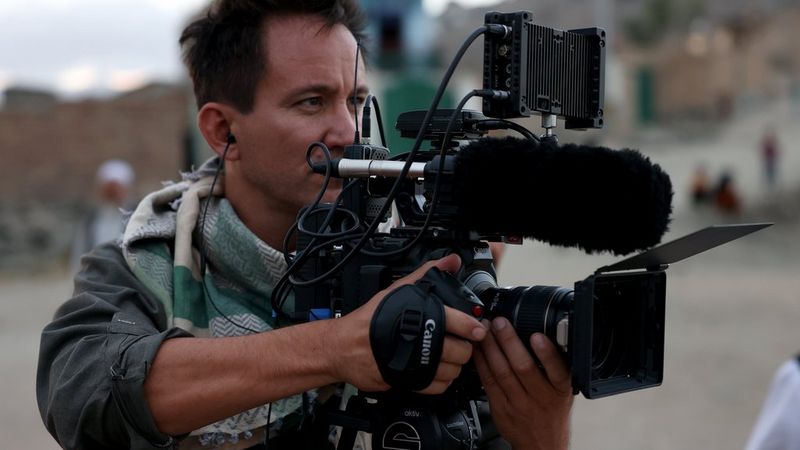 Documentary filmmaker Marcel Mettelsiefen holding a Canon camera.