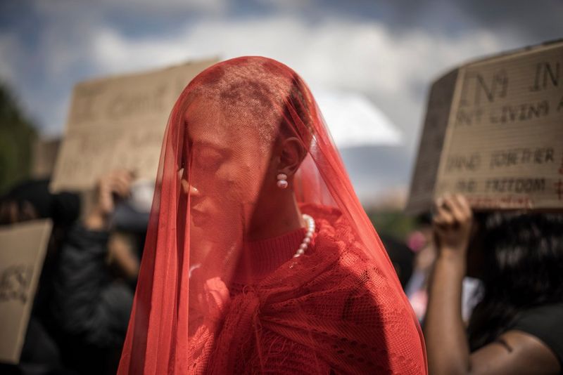 A woman with a red veil covering her head standing among a crowd of demonstrators holding placards.