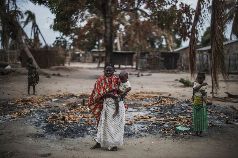 Une femme porte un jeune enfant dans ses bras, tandis que deux autres enfants se tiennent à ses côtés. Ils se trouvent dans une zone brûlée d'un village du Mozambique ayant récemment été attaqué.