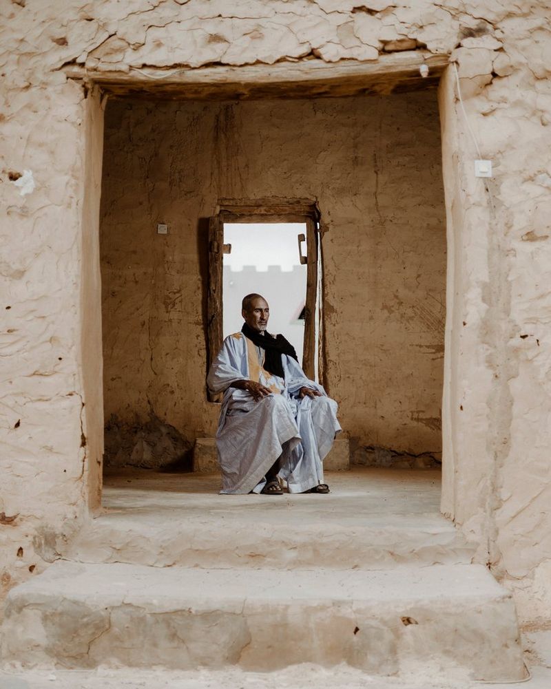 A portrait of a man seated in front of a window and framed by a stone door frame.