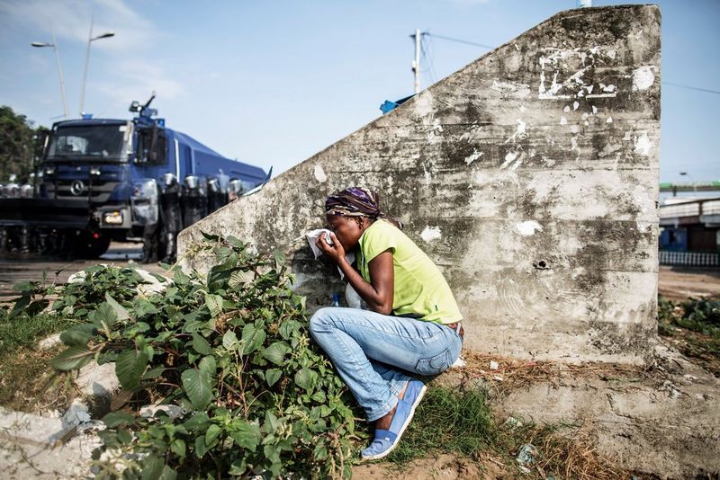 Une femme gabonaise accroupie derrière un mur se met à l'abri alors qu'un tank approche, tout en couvrant sa bouche avec un mouchoir.