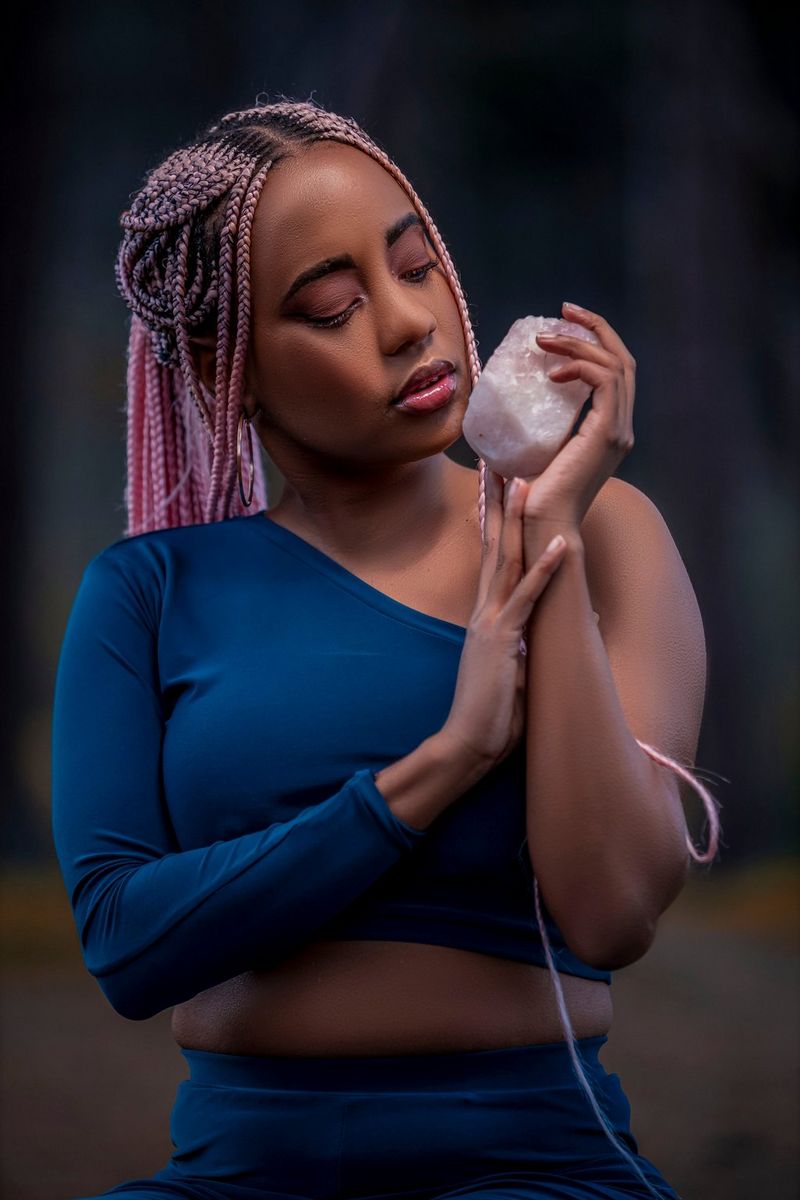 A portrait of a woman in a one shoulder blue top and pink hair, holding a Himalayan salt crystal in her hand. Taken on a Canon EOS R by Canon Ambassador Maropeng Vushangwe.