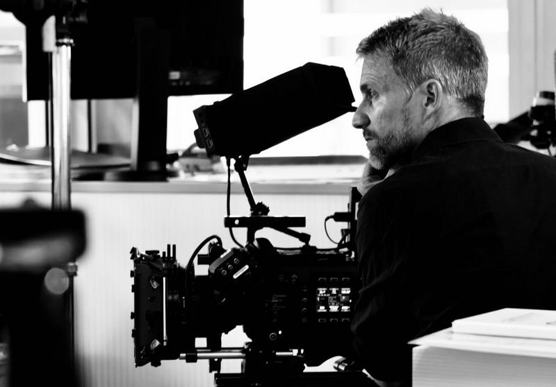 German cinematographer Martin Christ sits next to a Canon EOS C500 Mark II camera in a room filmed with technical equipment in this black and white image. 