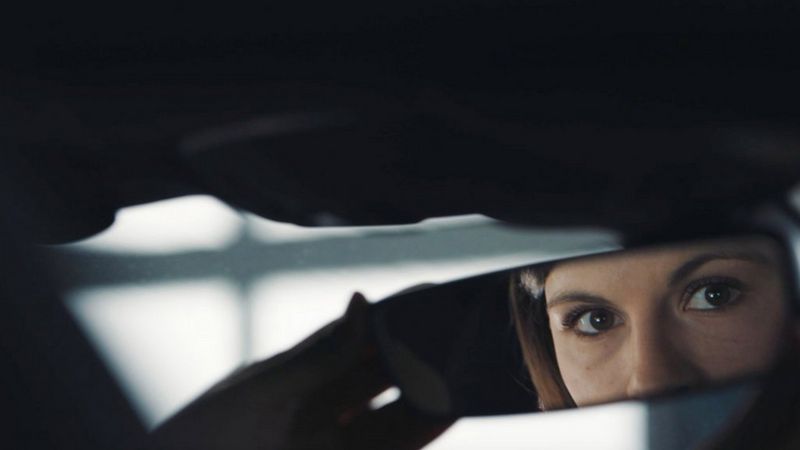 A woman's eyes and nose are reflected in the rearview mirror of a car in this still from a promotional film by cinematographer Martin Christ.