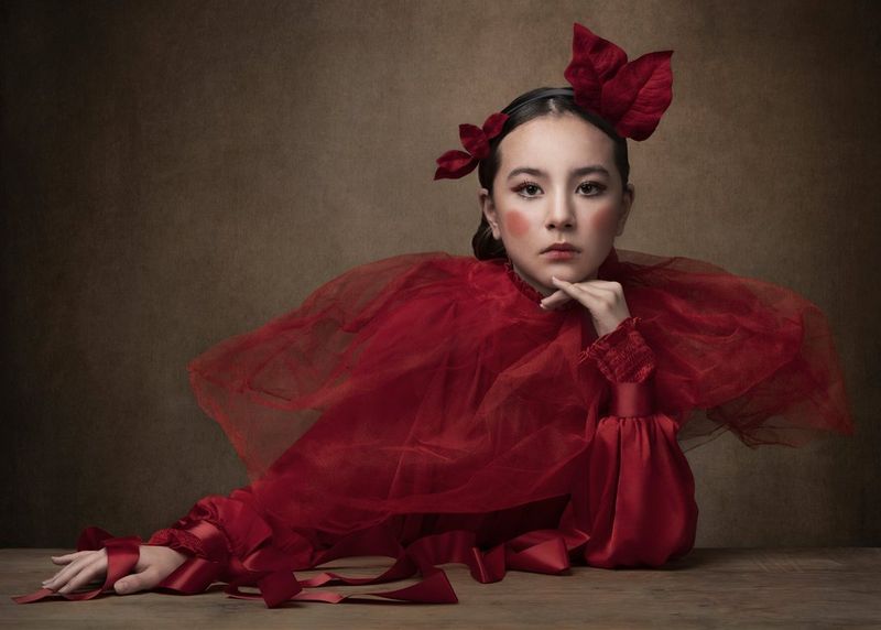 A portrait of a woman in a red satin dress with a large tulle collar and with red leaves in her hair, taken on a Canon EOS R5 by Martina Wärenfeldt. 