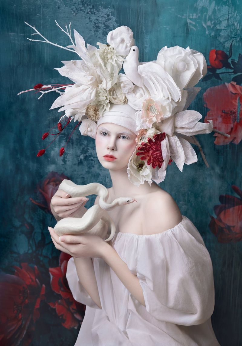 A painterly-style portrait of a young woman wearing an elaborate headdress and holding a white snake.