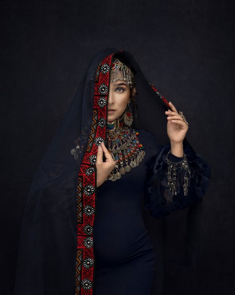A softly lit portrait of a woman wearing elaborate jewellery and holding a piece of embroidered fabric so it partially obscures her face, taken on a Canon EOS R5 by Martina Wärenfeldt.