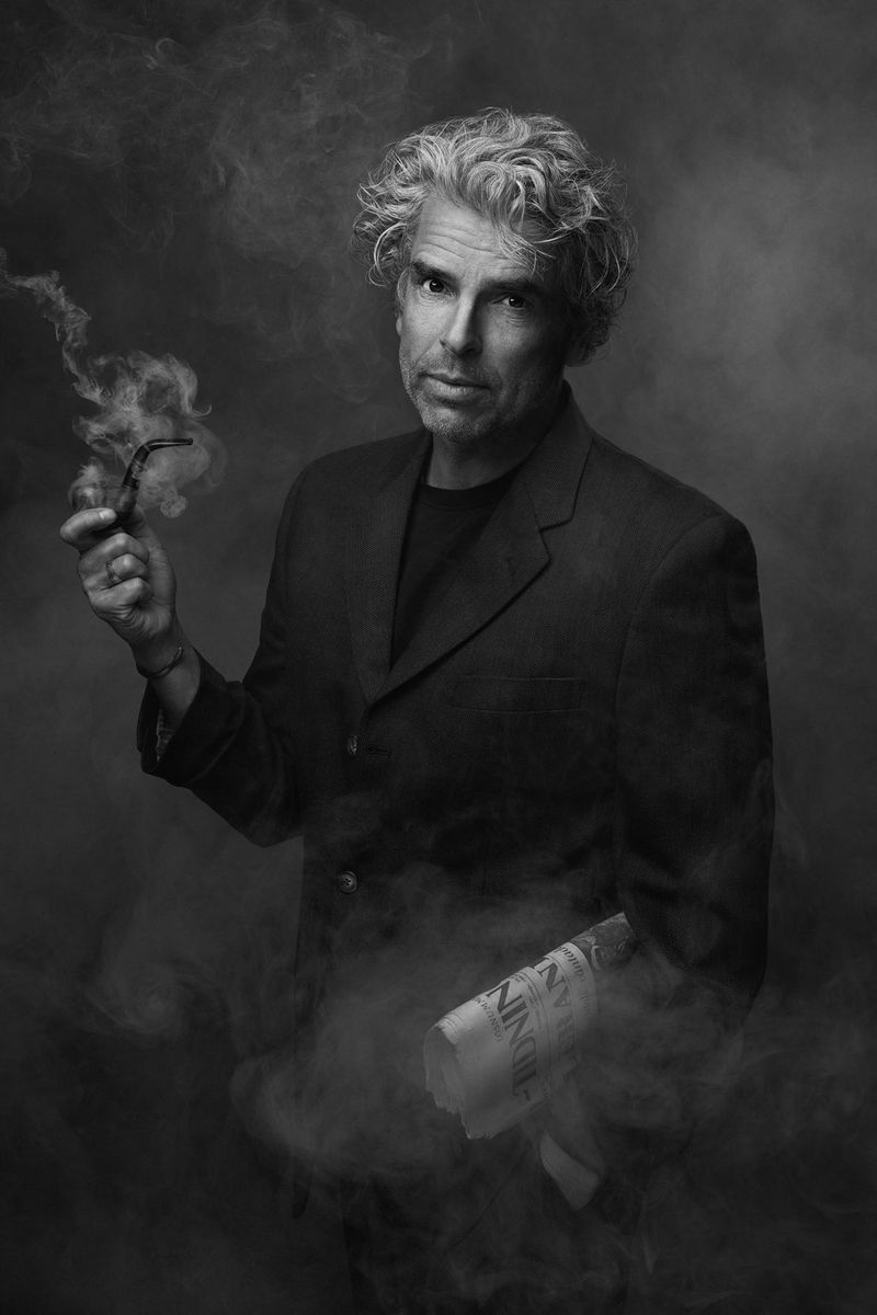 A softly lit black and white portrait of a man holding a pipe in one hand and a newspaper under his arm.