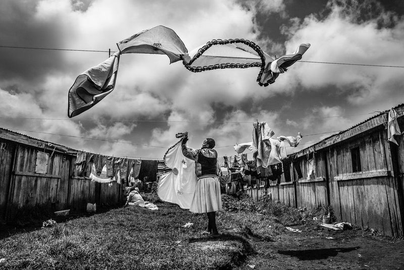 A black and white portrait of a woman hanging clothes on a washing line, which are billowing in the breeze, taken on a Canon EOS 5D Mark III by Canon Ambassador Meeri Koutaniemi.