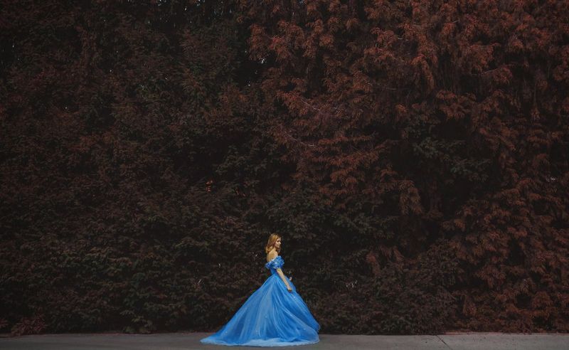 A model dressed in a Cinderella-esque blue dress stands in the leafy Royal Gardens at Prague Castle in the Czech Republic. 