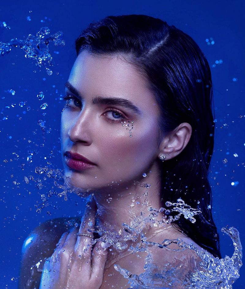 A model photographed against a blue backdrop with water droplets around her face, taken by Mor Tzidon on a Canon EOS R5.