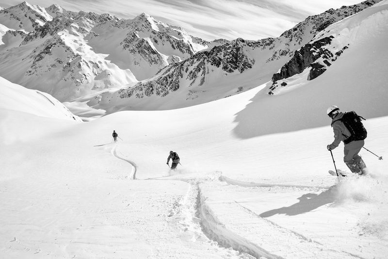 A black and white photograph of three people shot from behind, each about 30 metres apart, skiing down a mountain. In the background mountains stretch into the distance. Taken on a Canon EOS R by Nico Schaerer.