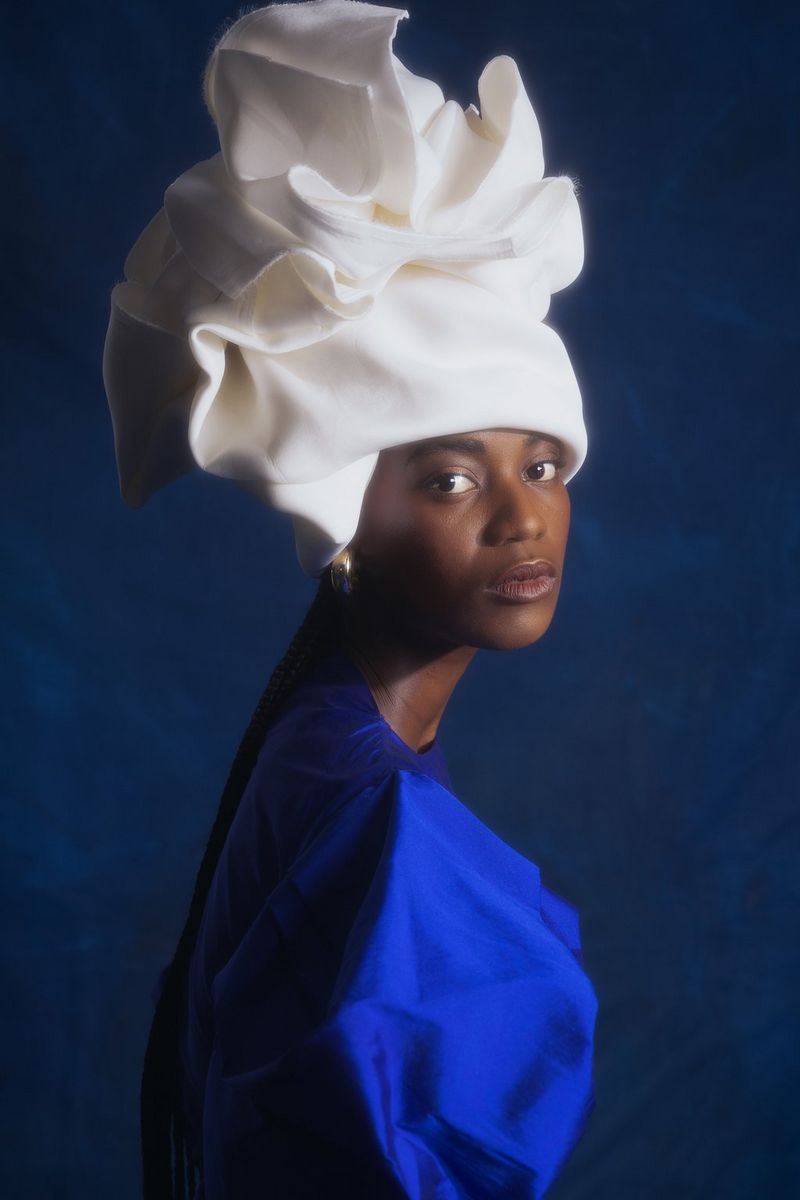 A model, shot from the side but with her face turned towards the camera, wearing an elaborately folded white headscarf and a bright blue dress. Taken by Nina Zimolong on a Canon EOS R5.