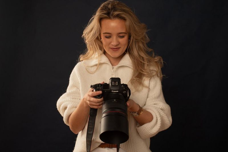 Fotograful de modă Nina Zimolong stând în faţa unui fundal întunecos, privind ecranul din spate al unui aparat foto Canon EOS R5 cu obiectiv RF 85mm F1.2L USM.
