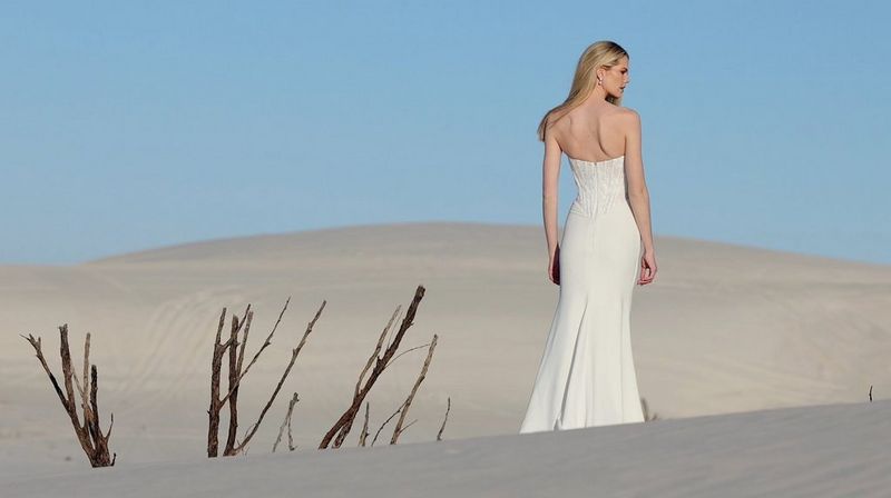 A woman with long blonde hair and wearing a long, white strapless dress standing in a desert. Still from a video for a fashion brand by Nina Zimolong.