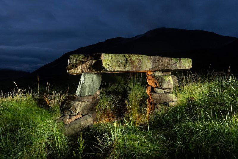 Illuminated stone ruins in a grassy setting, photographed at night with a long exposure.
