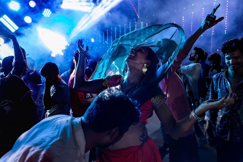 Revellers, with their arms raised, dancing in the street during a nighttime procession.