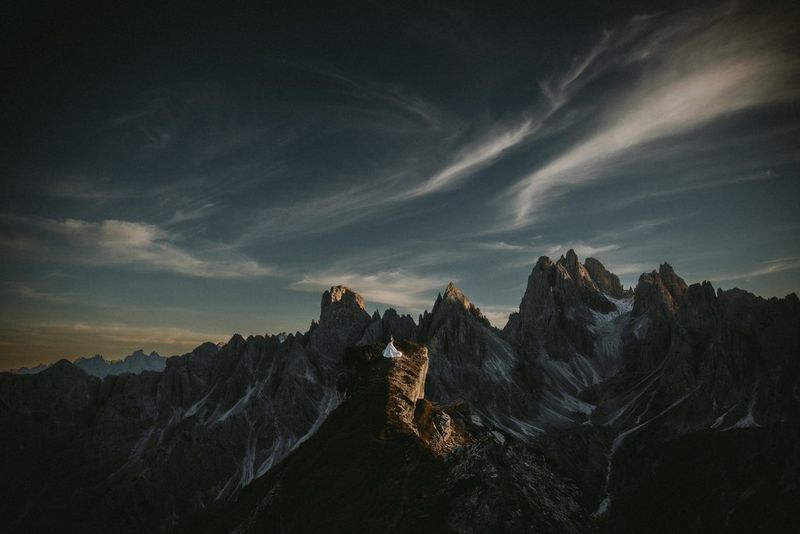 A bride and groom on top of a mountain, surrounded by jagged peaks and lit by the last of the day's sun. Taken on a Canon EOS R6 by Raïs De Weirdt.