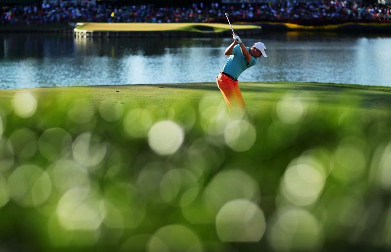 A golfer swings his arm back to take a shot as crowds watch from the banks of a lake behind him in a photo by Richard Heathcote/Getty Images.