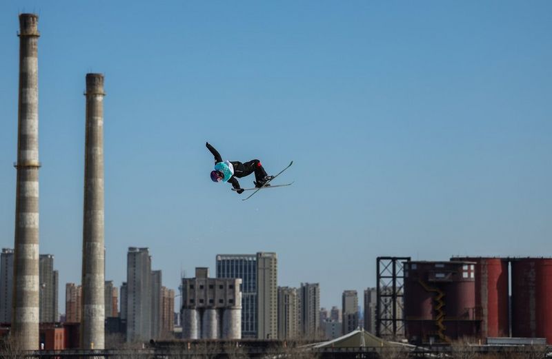 A skier performing a mid-air trick with tall chimneys and industrial buildings in the background in a photo by Richard Heathcote/Getty Images.