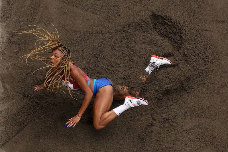 Shot from above, a long jumper lands in the sand pit, her long braids swinging around her head, in a photo by Richard Heathcote/Getty Images.