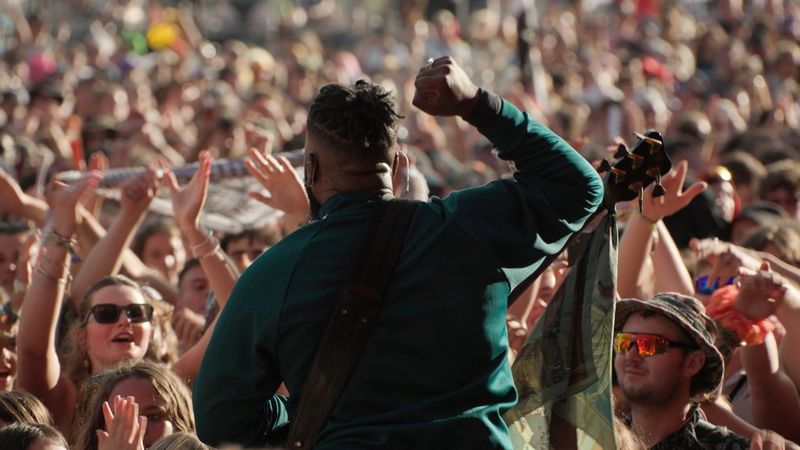 Shot from behind, an artist raises his arm as he performs in front of a large crowd. Still from a Boomtown video shot by Southpoint Films.