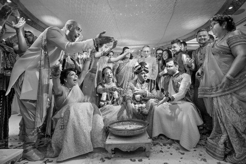 A family gather around a pot gesturing excitedly at each other, as the bride cheers and the groom pretends to look downcast.