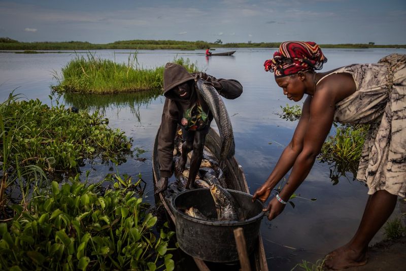 A woman collecting fish from a young man in a canoe.