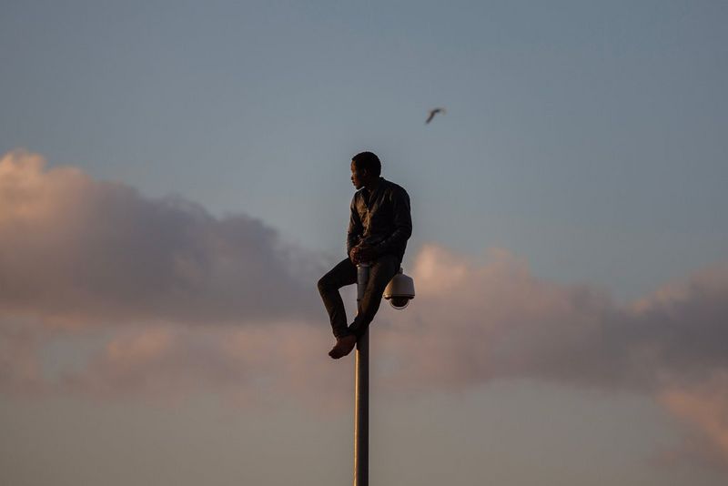 A young man sitting on top of a pole is silhouetted against a cloud-streaked sky. Taken on a Canon EOS 5D Mark III by Canon Ambassador Santi Palacios.