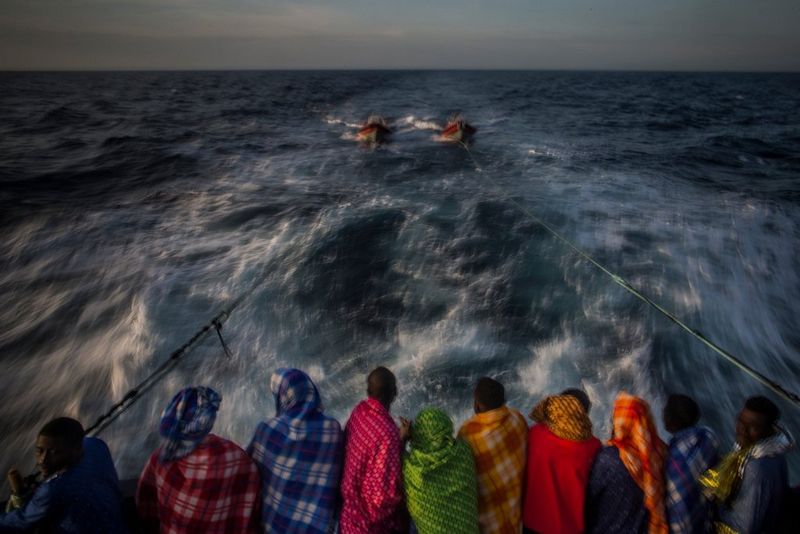 Refugees and migrants wrapped in colourful blankets look out to sea from the back of a rescue boat. Taken on a Canon EOS 5D Mark III by Canon Ambassador Santi Palacios.