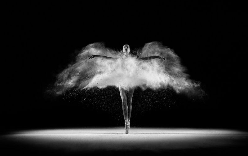 A black and white image of a ballet dancer frozen in motion. The addition of thrown white flour makes it look like she has wings. 