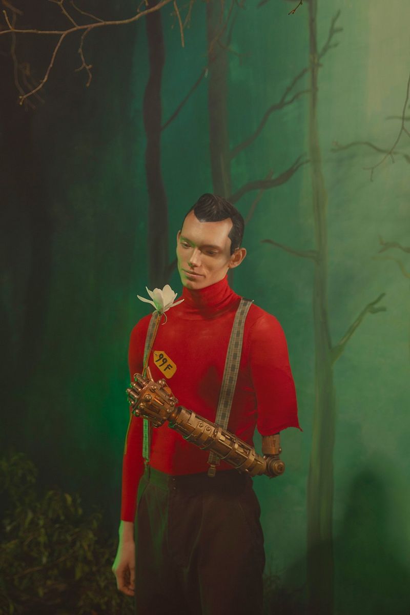 A stylised portrait of a figure with a robotic arm holding a white flower, against a backdrop of painted trees. Taken on a Canon EOS 5DS by Canon Ambassador Sébastien Salamand dit Le Turk.