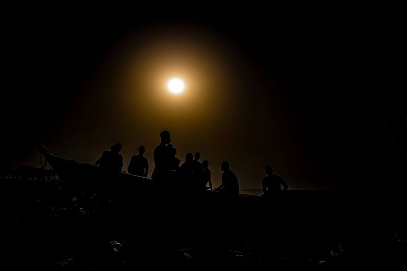 Silhouettes of figures standing in a boat as the moon shines above them, in a photo taken on a Canon EOS-1D X Mark III by Canon Ambassador Seibou Traoré.