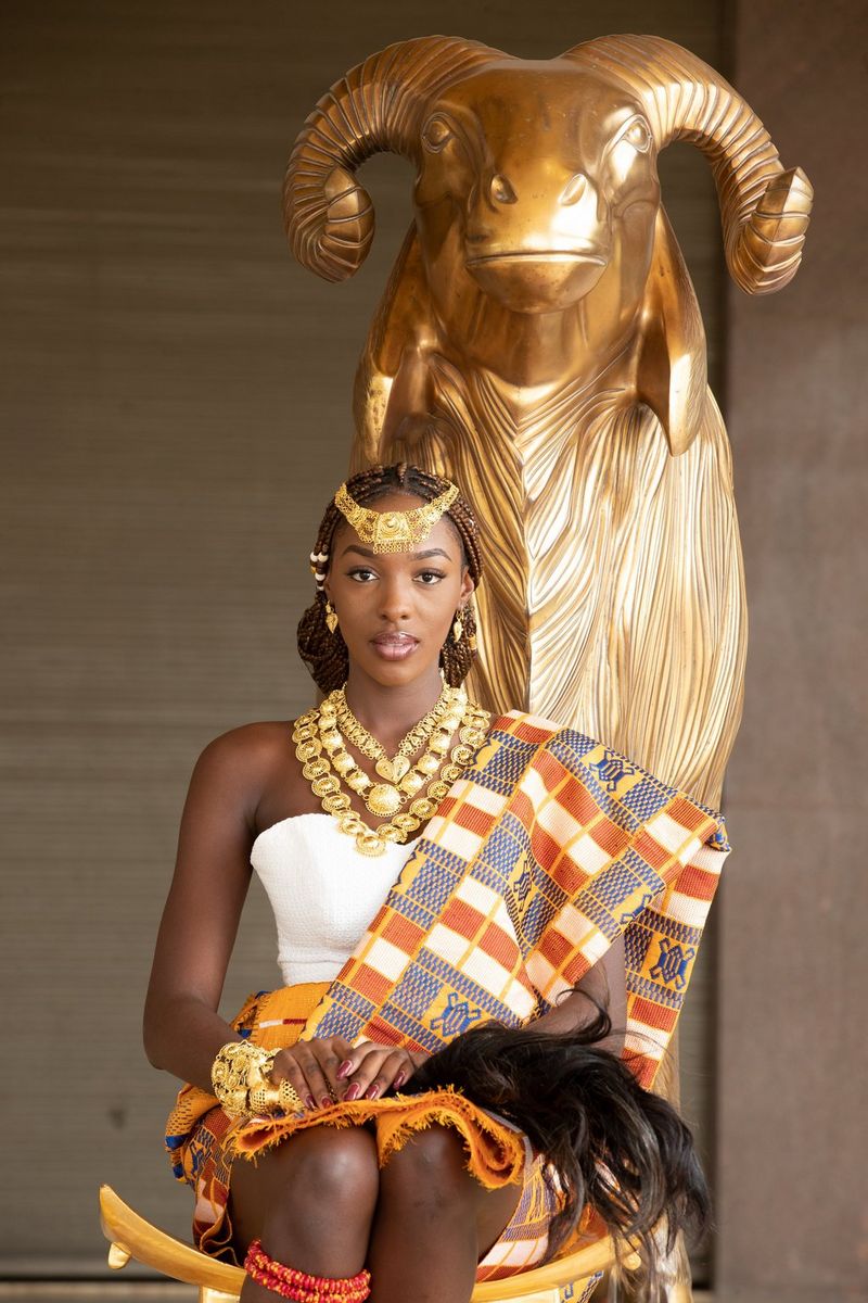 A portrait of Miss World Africa Olivia Yacé, adorned with gold jewellery and sitting on a chair in front of a golden statue of a ram. Taken on a Canon EOS-1D X Mark II by Canon Ambassador Seibou Traoré.