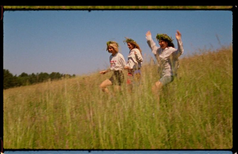 Three women wearing leaf crowns run down a grassy hill, in a still from a commercial shot with a film camera by Canon Ambassador Szymon Dudka.
