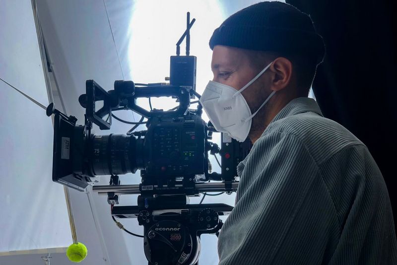 Canon Ambassador Szymon Dudka wearing a mask and standing in a studio behind a Canon EOS C500 Mark II camera.