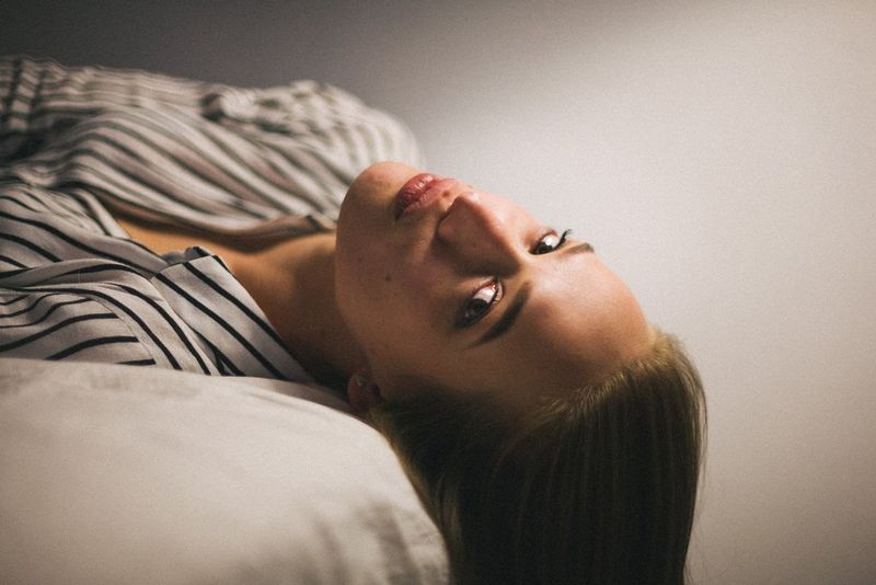 A portrait of a woman lying on a bed, her head slightly turned towards the camera, taken on a Canon EOS 5D by Canon Ambassador Szymon Dudka. 
