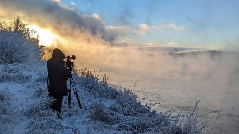 Canon Ambassador Tanya Aizikovich stands at a tripod with a Canon video camera in a snowy landscape, filming a scene for The Amazing Tale of the Peace River Meteorite.