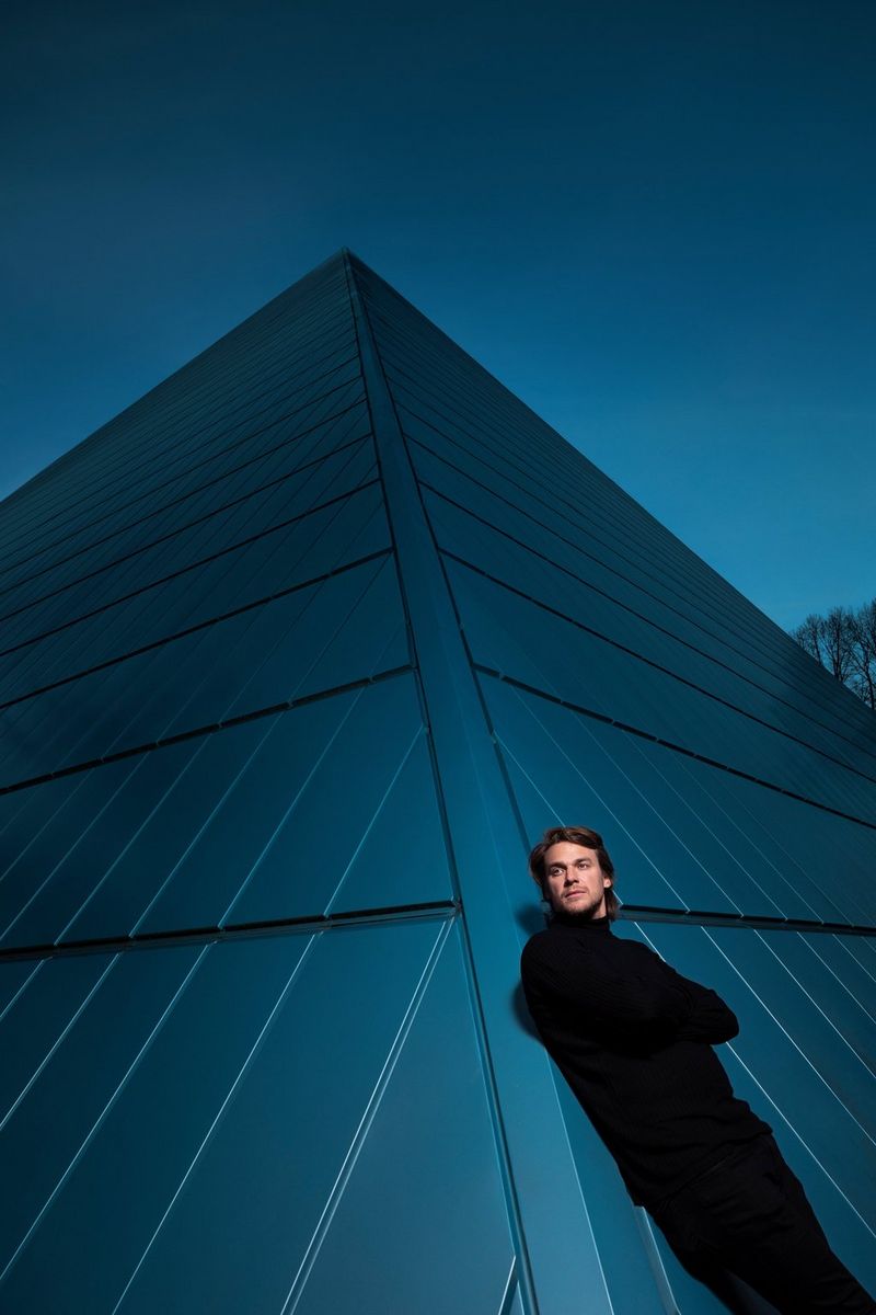 A portrait of Czech rapper Viktor Sheen, leaning over the edge of a red stairwell with the sky visible above him, taken on a Canon EOS R5 by Tomáš Třeštík.